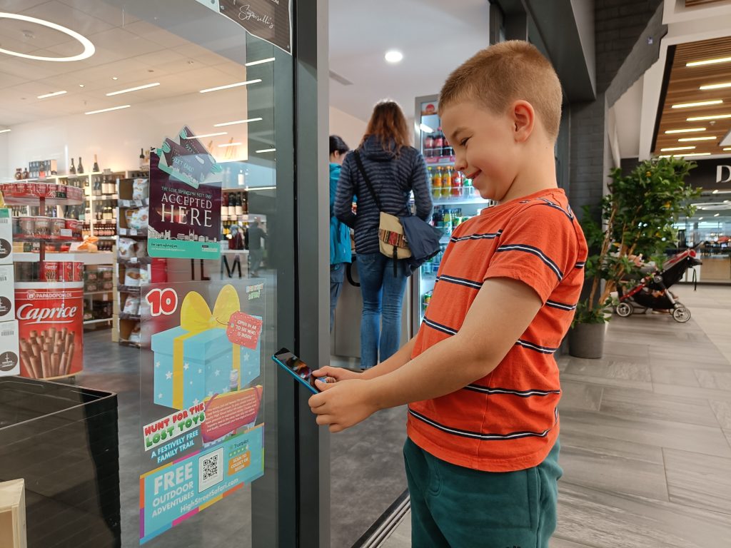 Boy scanning QR code in shop window to take part in Christmas trail.